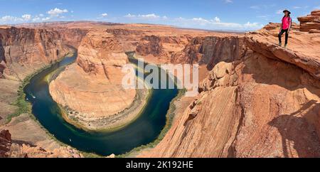 Junge Touristenin, die am sonnigen späten Morgen auf dem Grat des Horseshoe Bend am Colorado River in der Nähe von Page Arizona steht Stockfoto