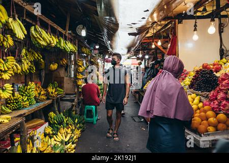 Junger Tourist, der in einer Gasse in Glodok Chinatown in jakarta Indonesia mit lokalen Straßenverkäufern, die Obst verkaufen, spaziert Stockfoto