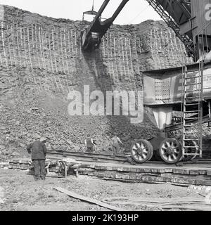 1950er Jahre, historisch, Entfernung von Ton aus einer riesigen Grube in der Ziegelei der London Brick Company, Bedford, England, Großbritannien. Arbeiter am Boden des Steinbruchs beobachten, wie der Bagger die Erde entfernt... Kein Schutzhelm in Sicht. Stockfoto