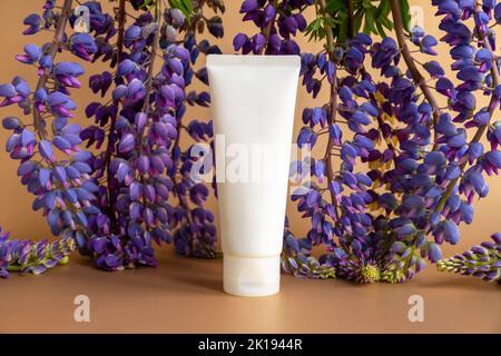 Mockup von weißen Squeeze-Flasche Plastikschlauch für Branding von Medizin oder Kosmetik - Creme, Gel, Hautpflege. Kosmetikflasche und Lupinenblumen Stockfoto