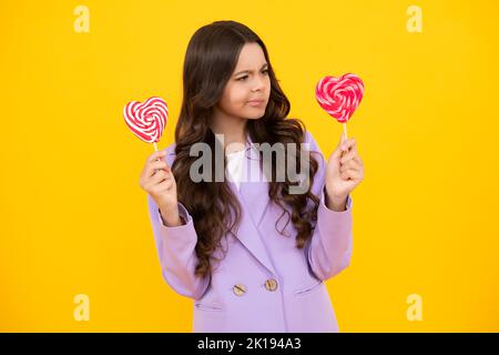 Lustiges Kind mit Lutscher auf gelbem isoliertem Hintergrund. Süßes Kindheitsleben. Teen Mädchen mit yummy Karamell Lollipop, Süßwarenladen. Lustiges Gesicht. Stockfoto