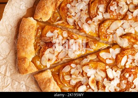 Nahaufnahme hausgemachter Kuchen mit Pflaumen und Mandelblättern auf Pergamentpapier. Draufsicht. Stockfoto