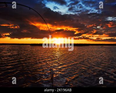 Angeln bei Sonnenuntergang. Raubfische beim Spinnen fangen. Sonnenuntergangsfarben auf der Wasseroberfläche, sonniger Weg von der niedrigen Sonne. Nerfling fing auf einem Spinner Stockfoto