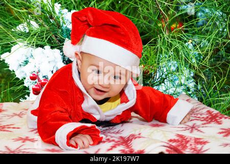 Niedliches Baby trägt zu weihnachten ein rotes weihnachtsmann-Kostüm auf einer Couch zu Hause, Stockfoto