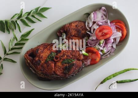 Knusprige Surmai-Fischbraten. Flacher, gebratener Königsfisch im Kerala-Stil serviert mit Zwiebeltomatensalat namens Challas. Aufgenommen auf weißem Hintergrund Stockfoto