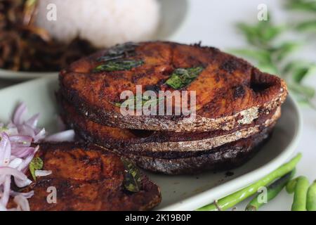 Knusprige Surmai-Fischbraten. Flacher, gebratener Königsfisch im Kerala-Stil, serviert mit Zwiebeltomatensalat namens Challas und weißem Reisgericht. Aufnahme auf weißem Hintergrund Stockfoto