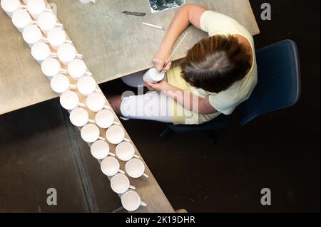 15. September 2022, Sachsen, Meißen: Die gekreuzten Schwerter, das Markenzeichen der Porzellan Manufaktur Meißen, werden mit einem Pinsel auf den Boden eines Bechers in der Feuerhalle der Porzellanmanufaktur Meissen gezogen. Foto: Sebastian Kahnert/dpa Stockfoto