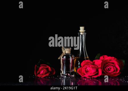 Parfümflaschen und rote Rosen auf schwarzem Hintergrund. Stockfoto