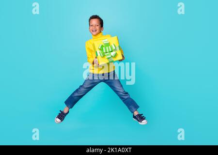 Ganzkörper-Foto von überglücklich aufgeregt Junge springen Hände halten giftbox isoliert auf türkisfarbenem Hintergrund Stockfoto