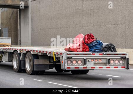Industrietaugliches großes Rig Langstrecken-Sattelschlepper, der aufgerollte Deckelplanen auf abwärts fahrenden Sattelaufliegern auf der mehrzeiligen Autobahn-Straße mit transportiert Stockfoto