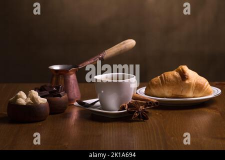 Kaffeetasse mit Jezve, Kaffeebohnen und Croissant auf einem Tisch Stockfoto