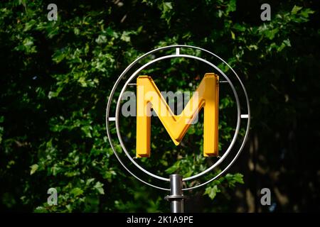 Die Abbildung zeigt ein Schild mit dem U-Bahn-Logo (gelbes Symbol) vor einer pariser U-Bahn-Station (Metropolitain) mit Bäumen im Hintergrund Stockfoto