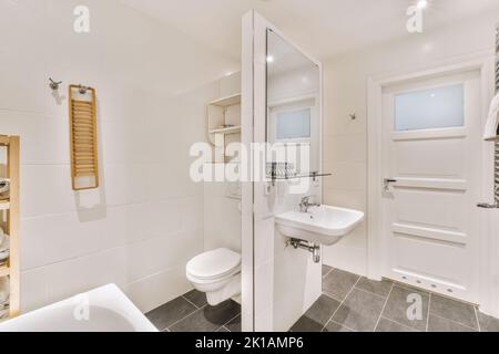 Waschbecken mit Spiegeln und sauberer Badewanne, Toilette im modernen Badezimmer mit weiß gefliesten Wänden Stockfoto