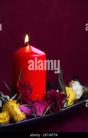 Kerze auf dunklem Hintergrund mit trockenen und verwelkten Rosen mit Kopierfläche oben anzünden Stockfoto