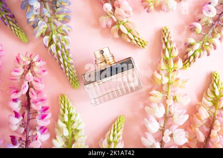 Unbranded vintage quadratische Parfüm Sprühflasche und rosa Lupinenblüten auf rosa Hintergrund. Vorderansicht oben, Sommerflachlage, Mockup, Schablone. Stockfoto