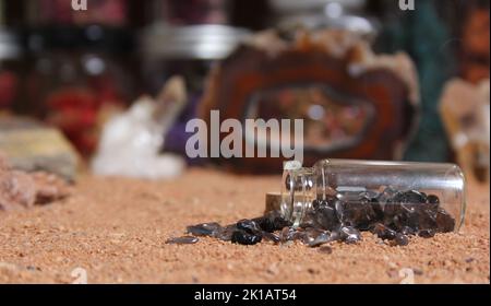 Flasche Chakra-Steine auf rotem Sand mit agatisierter Koralle im Hintergrund mit flachem Innengewinde Stockfoto