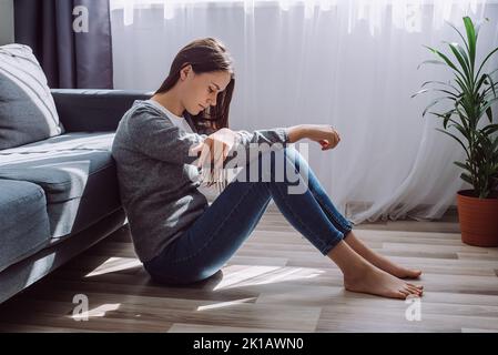 Depressiv traurig besorgt junge Brünette Frau allein auf dem Boden sitzen beunruhigt mit Einsamkeit, verärgert über Einsamkeit psychische Probleme, denken Sie an Abtreibung reg Stockfoto