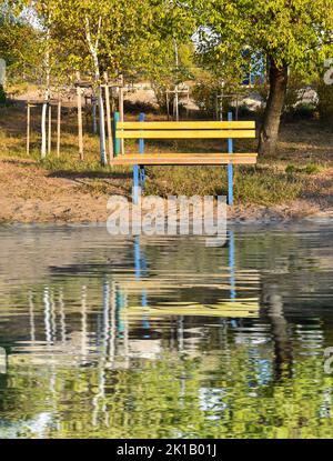 Eine gelbe Bank im Herbstpark spiegelt sich im Wasser wider. Schöner Herbsthintergrund. Konzept der Einsamkeit. Stockfoto