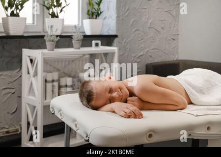 Kind nach Rückenmassage Behandlung in der Therapieklinik entspannend. Kid Body Treatment, Spa und Gesundheitskonzept. Schmerzlinderung. Humaner Rücken, Junge Wirbelsäule Kopie Stockfoto