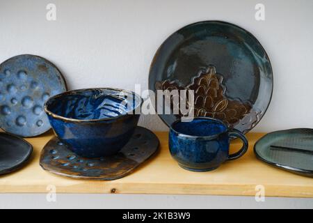 Keramik mit floralen und natürlichen Mustern im Regal des Ladens. Kreative, minimalistisch handgefertigte Tassen, Tassen und Teller. Töpferwaren Besteck irdischen Stockfoto