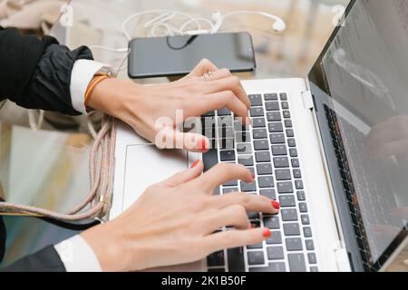 Seitenansicht Crop Hände von anonymen Weibchen in formal schwarz Anzug tippen auf Laptop-Tastatur, während am Tisch mit sitzen Smartphone während Telearbeit wo Stockfoto