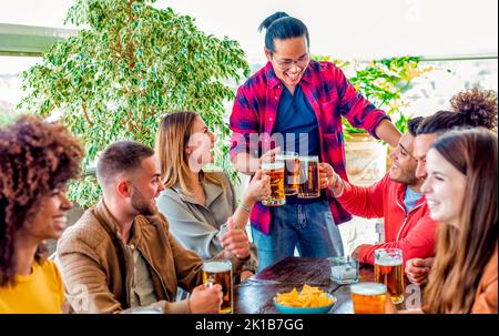 Internationale Gruppe von Freunden, die einen feierlichen Toast trinken Bier während der Happy Hour Urlaub. Menschen, die Spaß haben, lächeln und reden sitzen Stockfoto