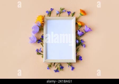 Blauer Bluebell, Blüten aus Logelien und Blüten aus orangefarbenen Ringelblumen mit weißem Textrahmen auf orangefarbenem Hintergrund. Sommer flach liegend Stockfoto