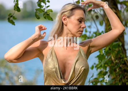 Attraktive blonde Frau in einem goldenen Go-Go-Kleid posiert vor der Kamera und streichelte ihr Haar Stockfoto