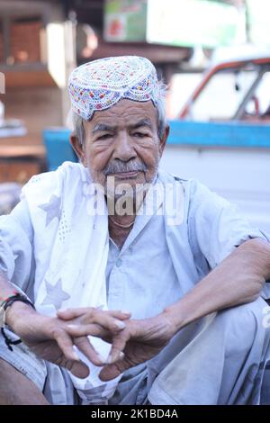 Ein vertikaler, flacher Fokus eines alten pakistanischen Mannes mit einem Schnurrbart in einem Topi, der auf der Straße sitzt Stockfoto