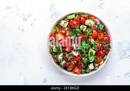 Quinoa Tabbouleh Salat mit Tomaten, Paprika, Avocado, Gurken und Petersilie. Traditionelles nahöstliches und arabisches Gericht. Weißer Küchentisch im Hintergrund Stockfoto