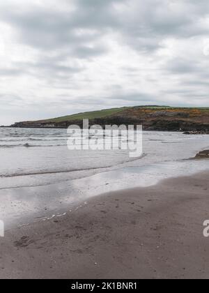 Blick auf den Rosscarbery Pier vom Warren Beach, Südküste Irlands. Wellen an einem Sandstrand. Der Atlantik bei bewölktem Wetter. Stockfoto