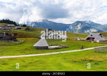 Frau Touristin auf einem Mountainbike, Radfahren auf einer Velika planina Almwiese, mit traditionellen Holzhütten, kamnik, Slowenien Stockfoto