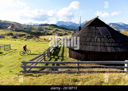 Ein Mountainbiker auf einer Radtour auf dem Velika Planina Plateau in der Nähe von Kamnik, mit Halt am traditionellen Hirtenhaus aus Holz, Slowenien Stockfoto