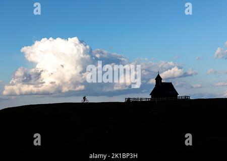 Eine Mountainbike-Tour zum Abschluss einer Radtour bei Sonnenuntergang zur hölzernen Kapelle Maria des Schnees auf dem Velika Planina Plateau bei Kamnik, Slowenien Stockfoto