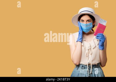 Reiseverbot. Sommerurlaub. Covid-19-Beschränkung. Schockierte Frau in Schutzmaskenhandschuhen mit ausweisen, die die Kamera isoliert auf Beige ansahen Stockfoto