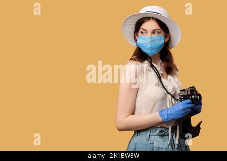 Halten Sie Reisemomente fest. Covid-19-Beschränkung. Abstand halten. Besorgte Frau in Schutzmaske Handschuhe halten Retro-Kamera Blick zurück Kopie Raum isol Stockfoto