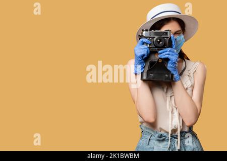 Reisefoto. Pandemiemaßnahmen. Halten Sie Urlaubserinnerungen fest. Frau in Schutzmasken-Handschuhen, die auf einer Retro-Kamera fotografieren, isoliert auf beigefarbenem Kopierraum Stockfoto