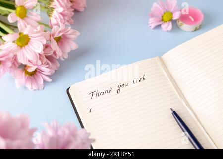 Handgeschriebene Worte Dankesliste in einem persönlichen Tagebuch auf hellblauem Hintergrund mit rosa Blumen. Konzept des Danksagung-Journals Stockfoto