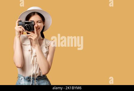 Urlaubsreise. Halten Sie Erinnerungen fest. Reisefoto. Glückliche Frau Strohhut, die auf einer Retro-Kamera fotografiert, isoliert auf beigem Kopierraum. Werbung nach hinten Stockfoto