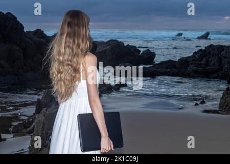 Junge attraktive Frau in Kleid, arbeiten auf Laptop. Unabhängiges Arbeitermädchen. Digitales Nomadenkonzept Stockfoto