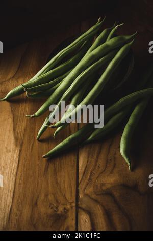 Grüne Bohnen auf einer hölzernen Oberfläche, auch als französische Bohnen, Schnur-Bohnen oder Druckknöpfe bekannt, frisch geerntetes Gemüse vor dunklem launischem Hintergrund Stockfoto