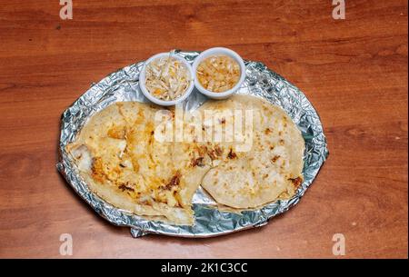 Zwei nicaraguanische Pupusas mit Salat auf dem Tisch. Köstliche salvadorianische Pupusas mit geschmolzenem Käse auf dem Tisch serviert. Traditionelle Pupusas Stockfoto