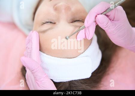 Kosmetikerin reinigt Mädchen Stirn mit uno Löffel in Kosmetologie Klinik Stockfoto