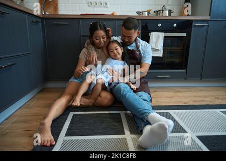 Mädchen sonnt sich in den Armen ihrer Eltern Stockfoto