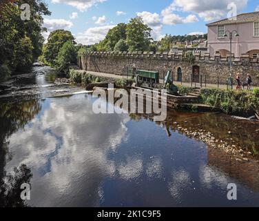 Das Weir am Fluss Tavy bei Tavistock von der Brücke aus gesehen mit Reflexen des Himmels. Die historischen Mauern und der Fluss gehen in Richtung Meadows al Stockfoto