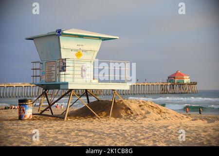 Ein Rettungsschwimmer Turm an einem kalifornischen Strand bei Sonnenuntergang. Weit dahinter liegt der Huntington Beach Pier Stockfoto