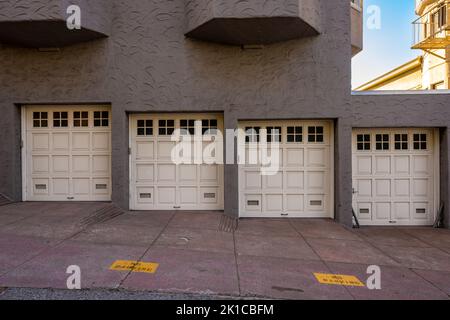 Stuckgebäude mit vier Garagentüren, die in San Francisco den Hügel hinunter führen Stockfoto