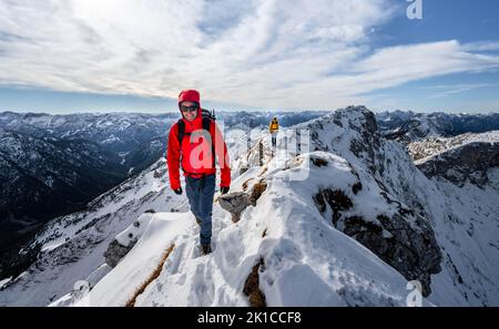 Zwei Bergsteiger auf einem schmalen felsigen, schneebedeckten Bergrücken, hinter Gipfelkrähen, Blick auf das Bergpanorama, Wanderung zur Ammergauer Hochplatte, im Herbst Ammergau Stockfoto
