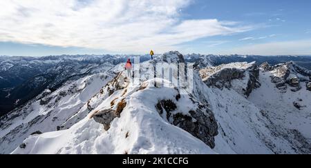 Zwei Bergsteiger auf einem schmalen felsigen, schneebedeckten Bergrücken, hinter Gipfelkrähen, Blick auf das Bergpanorama, Wanderung zur Ammergauer Hochplatte, im Herbst Ammergau Stockfoto