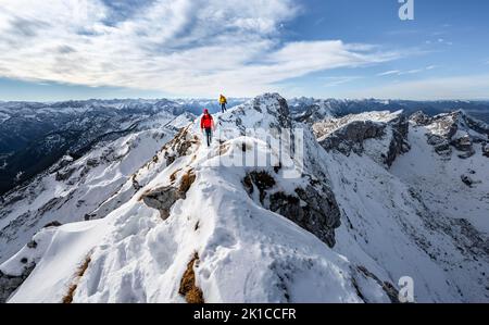 Zwei Bergsteiger auf einem schmalen felsigen, schneebedeckten Bergrücken, hinter Gipfelkrähen, Blick auf das Bergpanorama, Wanderung zur Ammergauer Hochplatte, im Herbst Ammergau Stockfoto